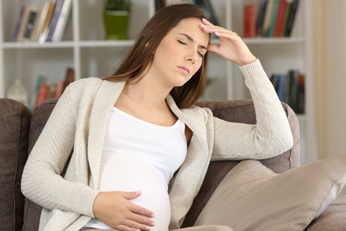 Pregnant woman suffering migraine sitting on a sofa at home
